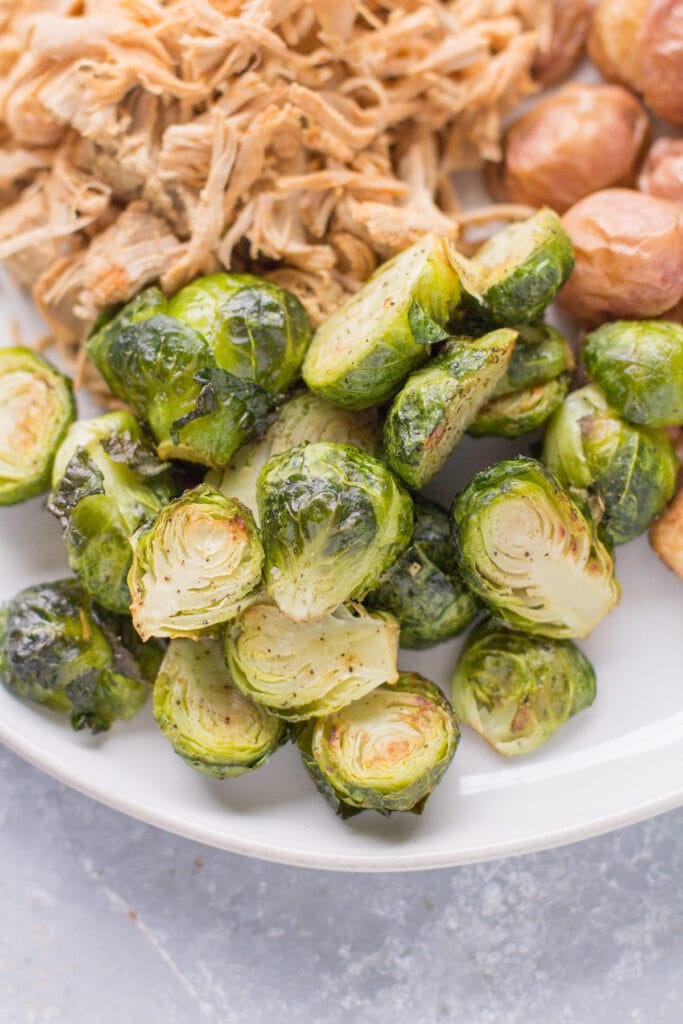 Roasted brussels sprouts on a plate with pulled pork and crispy potatoes.