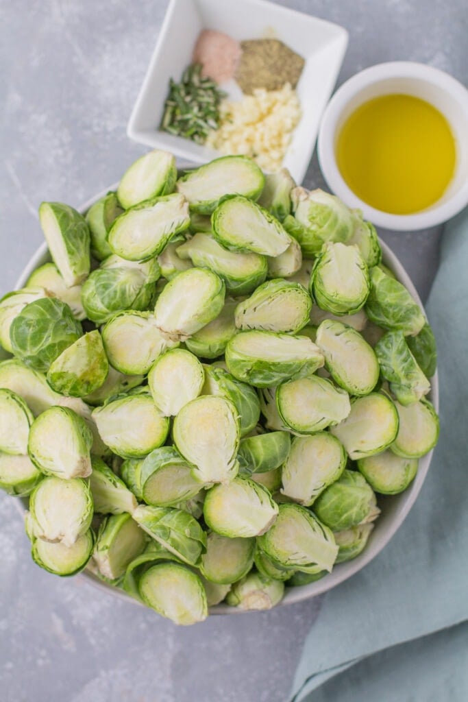 ingredients for Garlic Roasted Brussels Sprouts - halved brussels sprouts, olive oil, fresh garlic, salt and pepper, fresh rosemary laid out in small white bowls