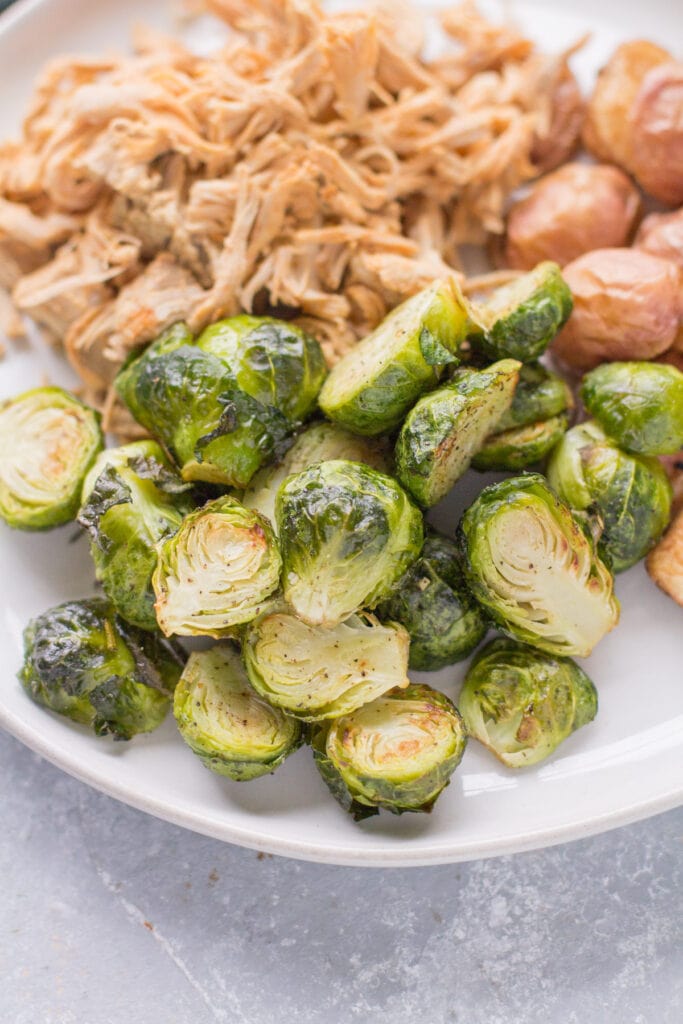 Roasted Brussels Sprouts with garlic on a plate ready to be eaten with whole30 pulled pork and roasted potatoes