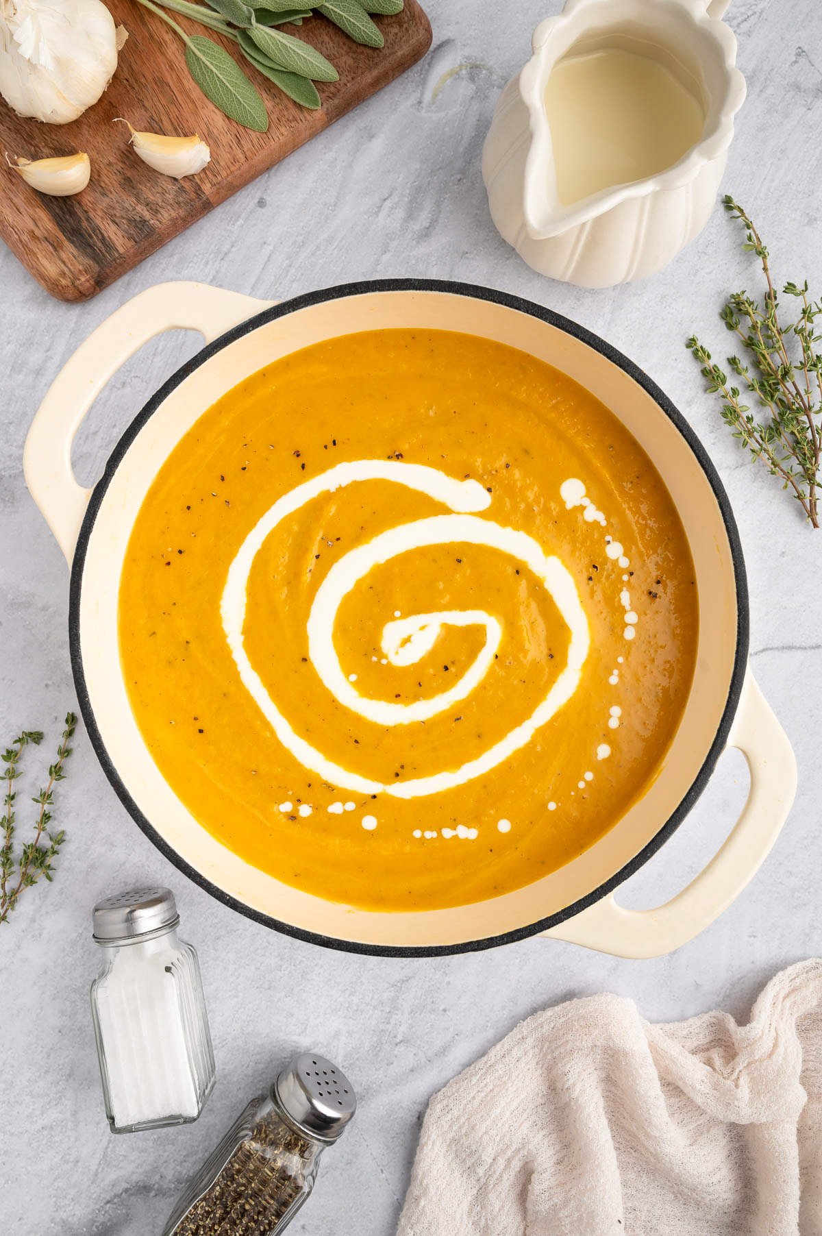 An overhead shot of a pot of butternut squash soup with a swirl of milk on a grey background