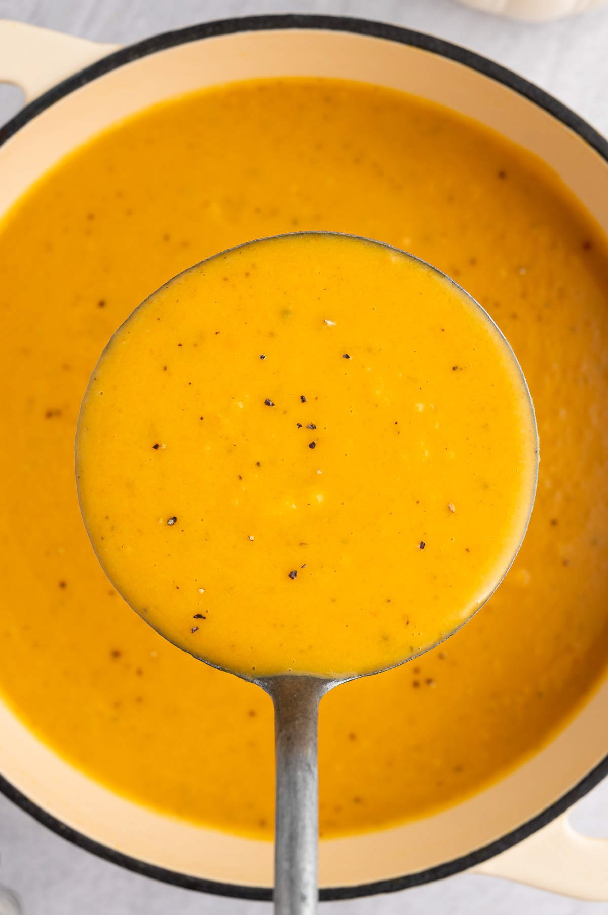 A ladle taking a large scoop of roasted butternut squash soup out of a pot