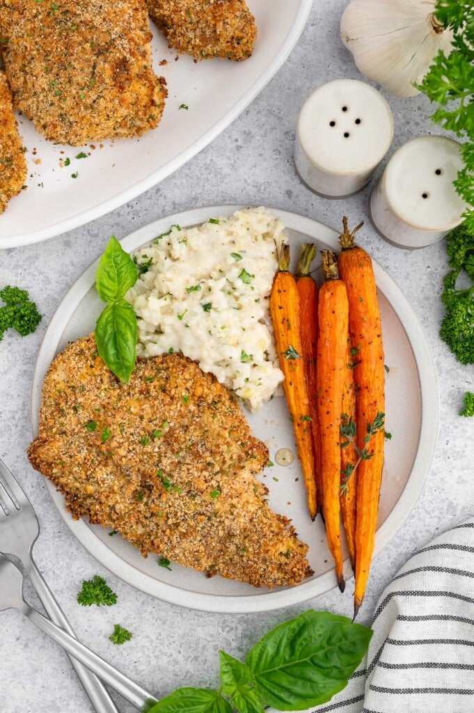 A plate with honey roasted carrots, a baked chicken cutlet, and lemon risotto with a plate of more cutlets on the side.