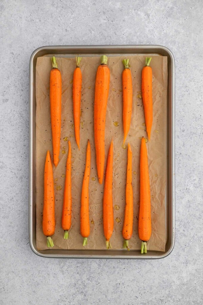 Raw carrots on a parchment lined baking sheet.