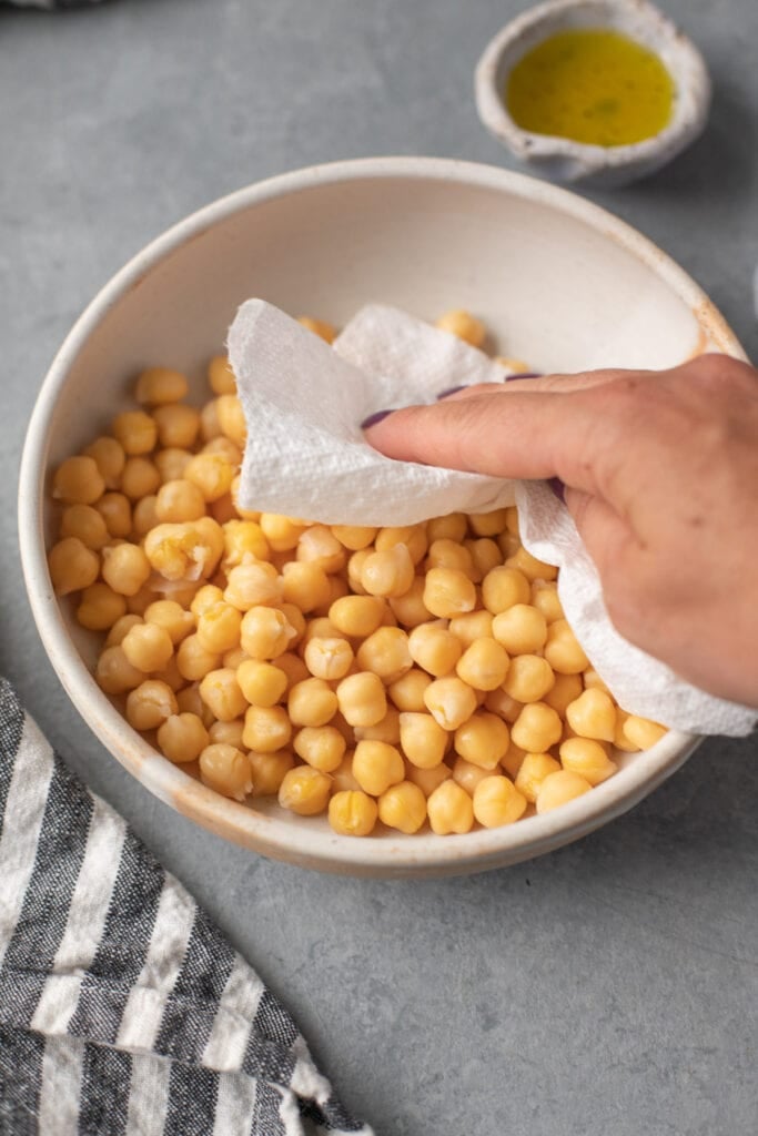 a hand patting chickpeas in a bowl dry with a paper towel