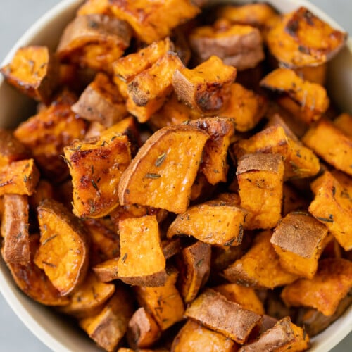 A white bowl of roasted sweet potato cubes on a grey background