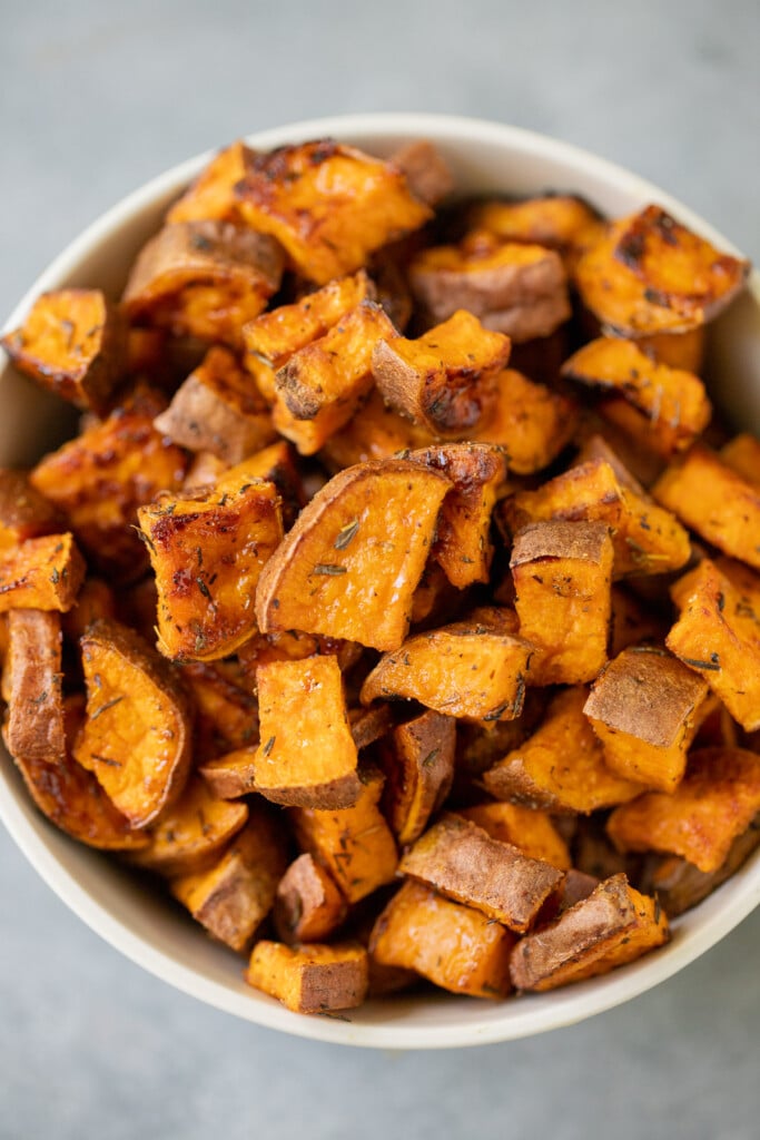 A white bowl of roasted sweet potato cubes on a grey background