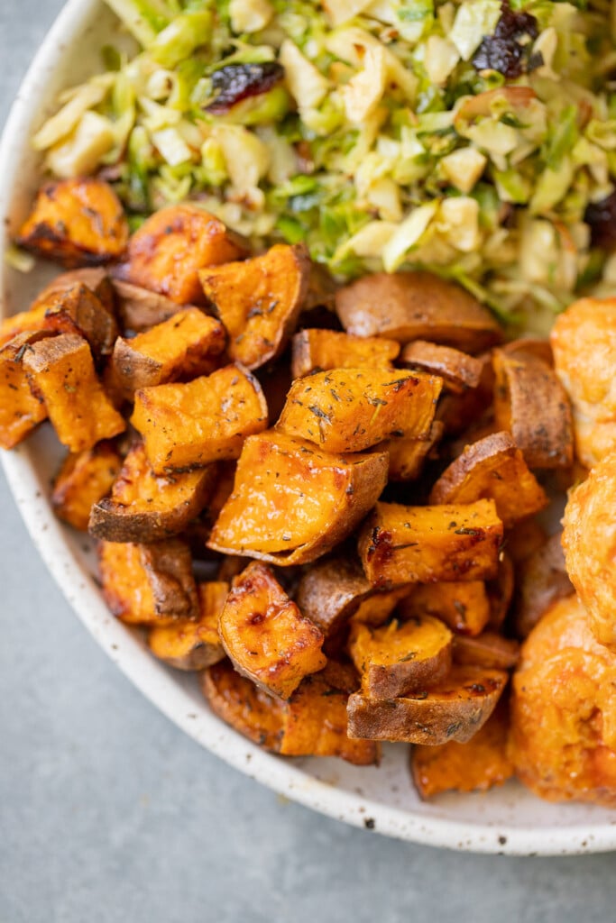 Roasted sweet potato cubes on a white plate with a salad and meatballs on the side