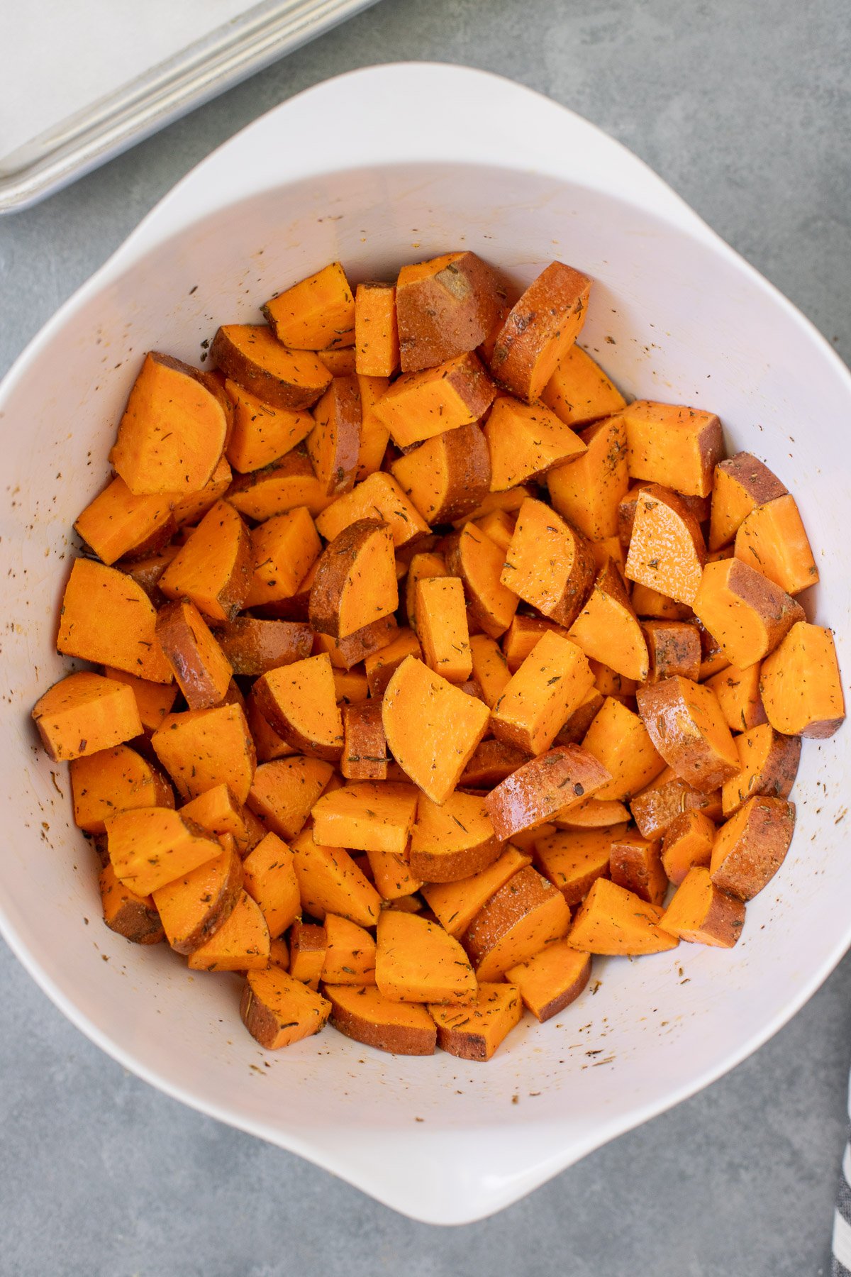 Cubed sweet potatoes in a white bowl after being tossed in oil and spices before being cooked