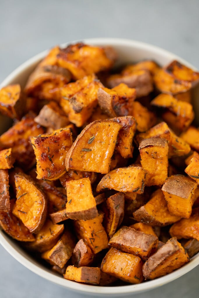 A white bowl of roasted sweet potato cubes on a grey background