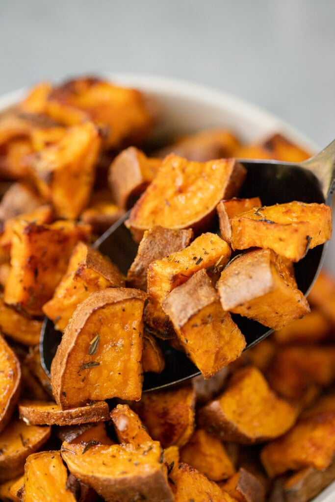 A spoon taking a spoonful of cubed sweet potatoes out of a bowl of potatoes