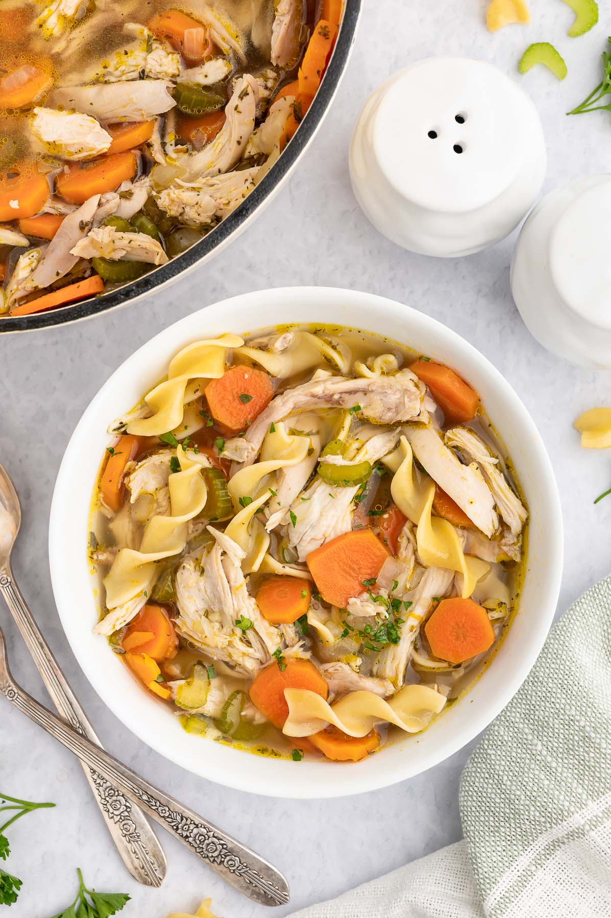 A white bowl of rotisserie chicken soup with the dutch oven of the soup on the side on a marble counter