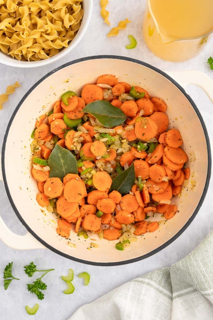 A dutch oven with celery, onion, garlic, carrots, spices cooking to make rotisserie chicken soup on a white background