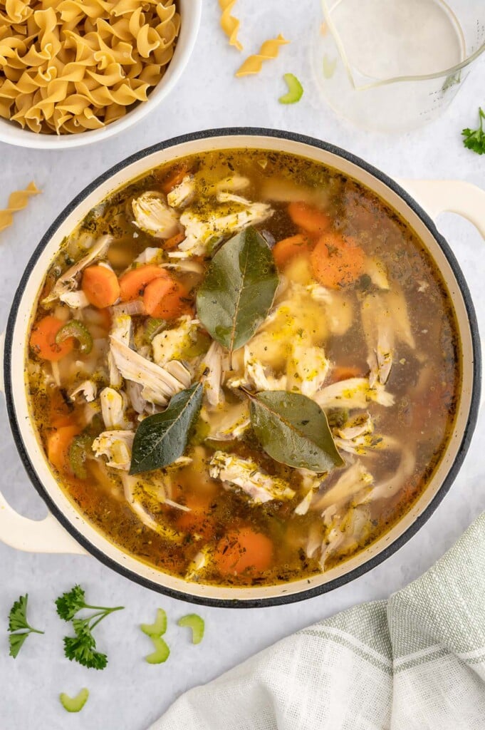 All ingredients (except egg noddles) for rotisserie chicken soup in a dutch oven before fully cooking with a bowl of egg noddles on the side