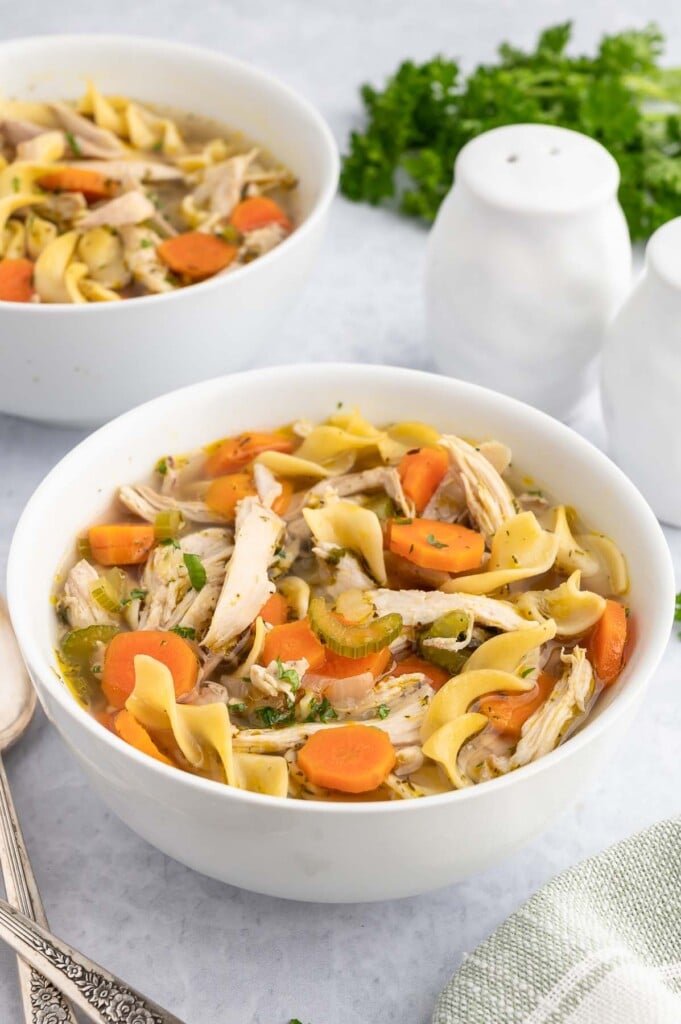 rotisserie chicken soup in a white bowl with another bowl of soup in the background