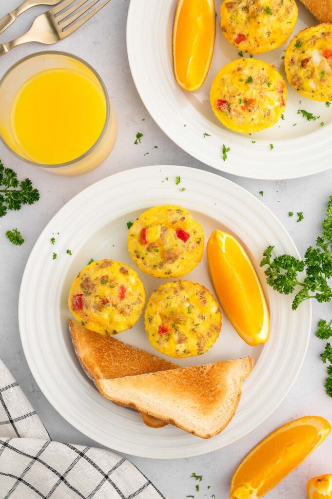 A white plate with three sausage egg muffin cups, an orange slice and toast on it.