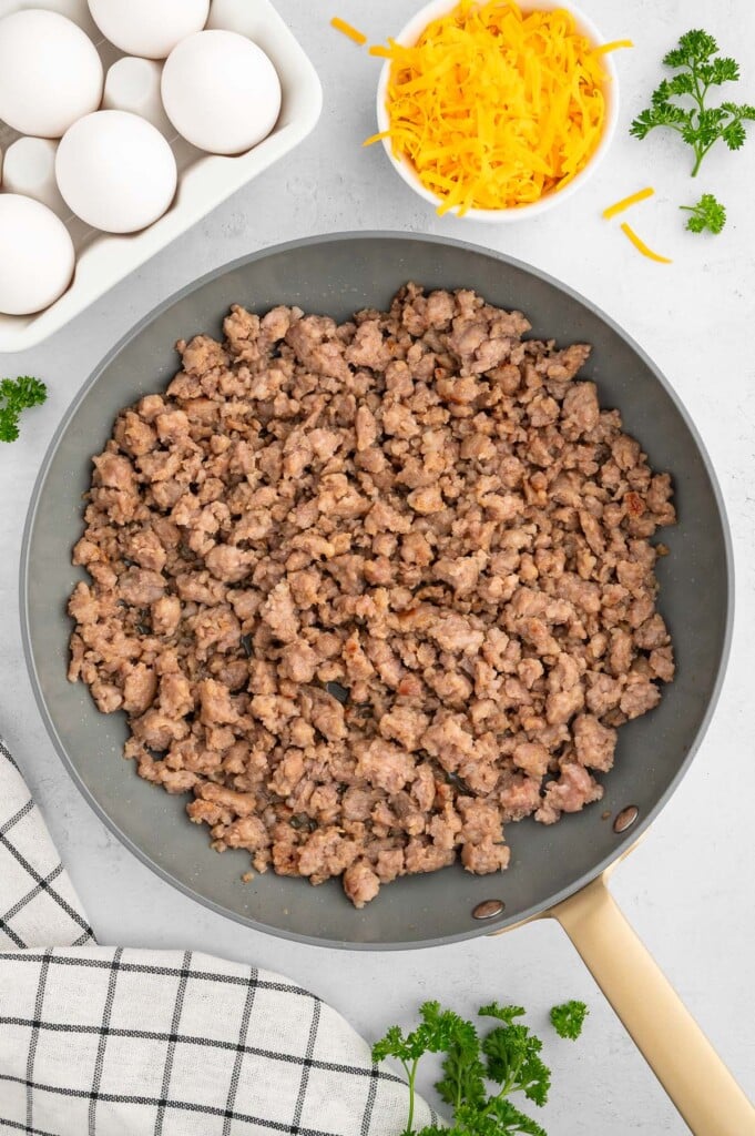 Browned sausage in a pan with eggs and cheese on the side.