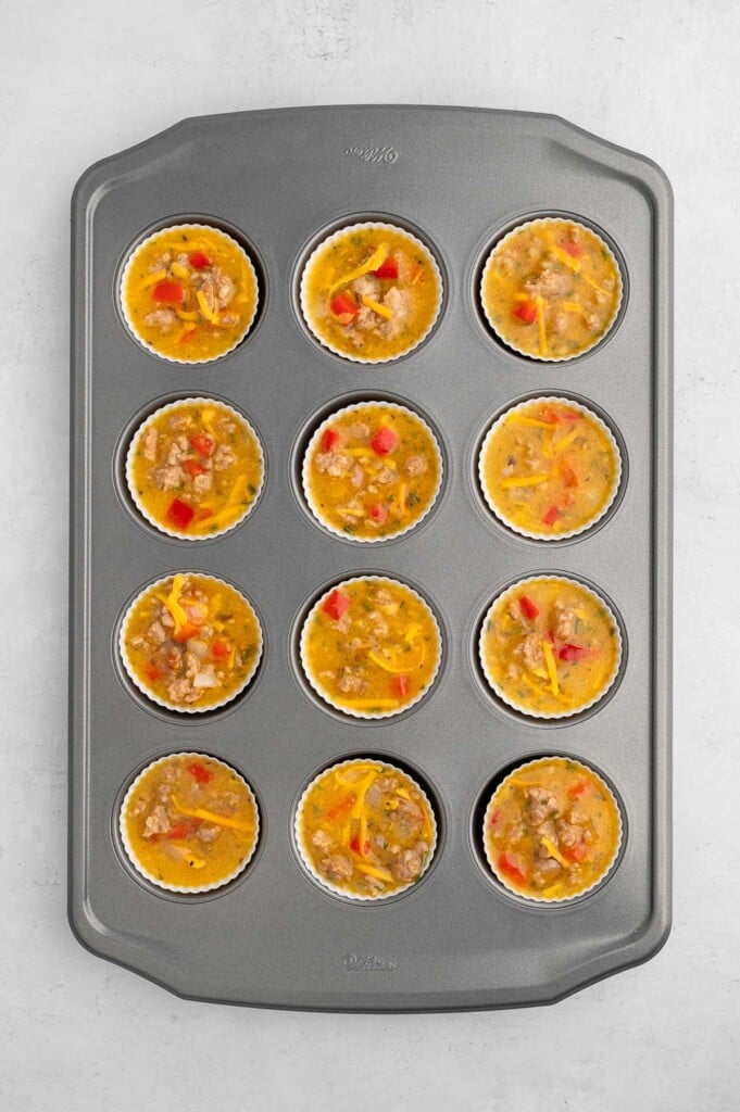 Uncooked sausage egg muffin cups in a lined muffin tin. 