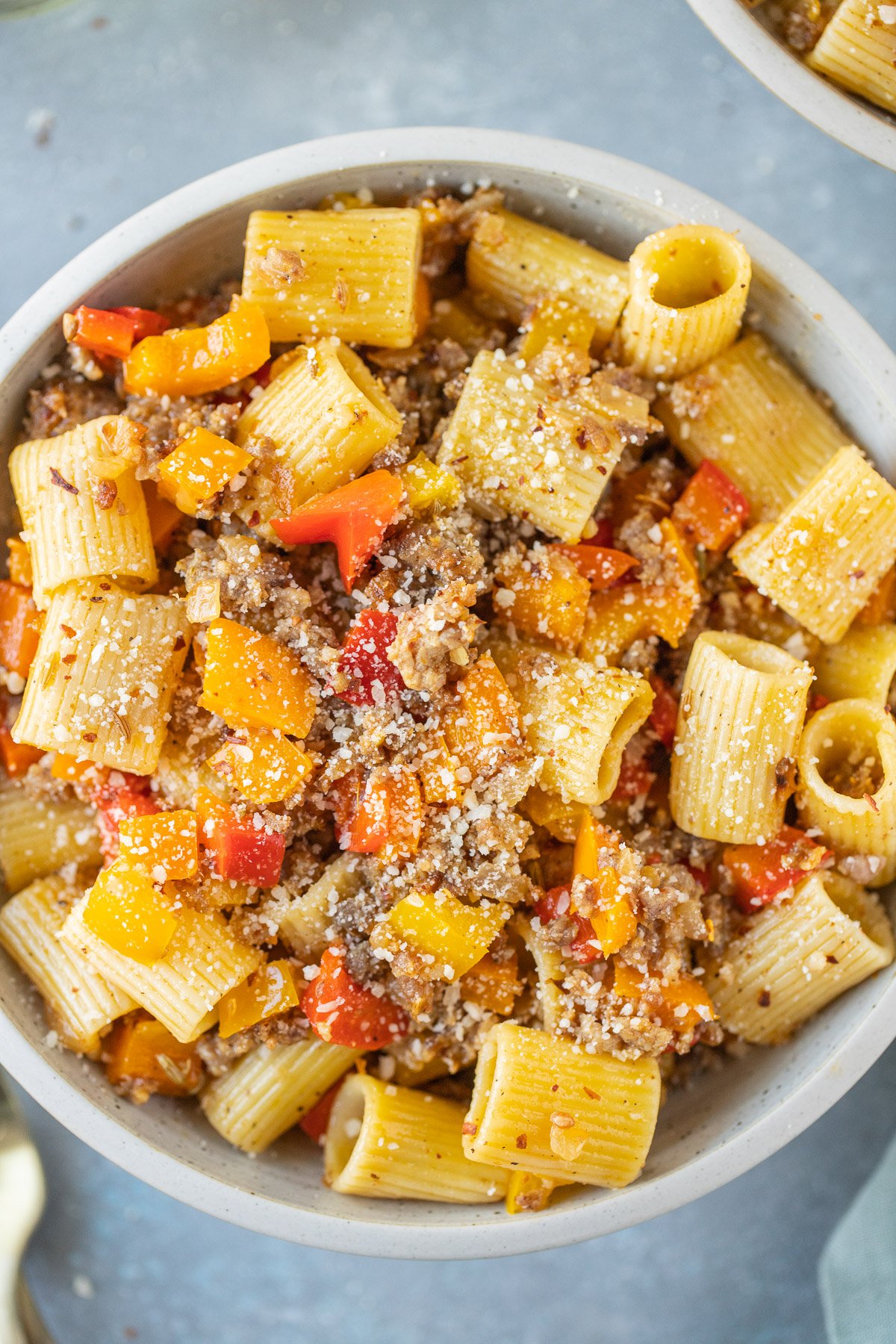 An overhead shot of a bowl of sausage and peppers pasta on a grey background