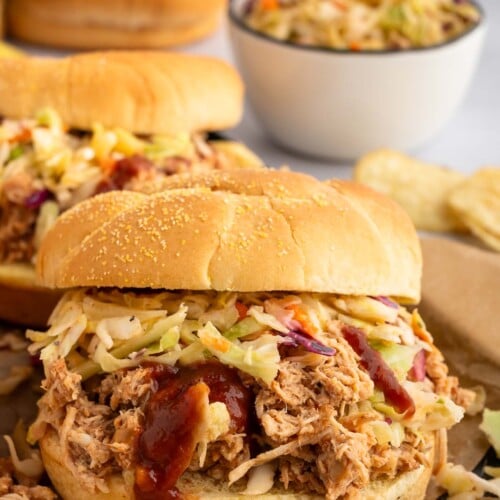A Slow Cooker BBQ Chicken sandwich with cole slaw in the background.