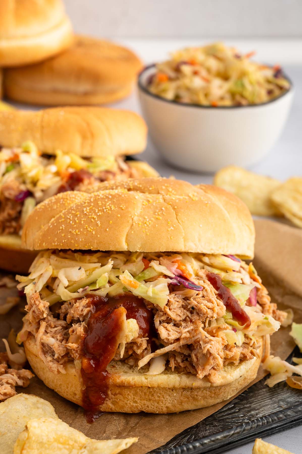 A Slow Cooker BBQ Chicken sandwich with cole slaw in the background.