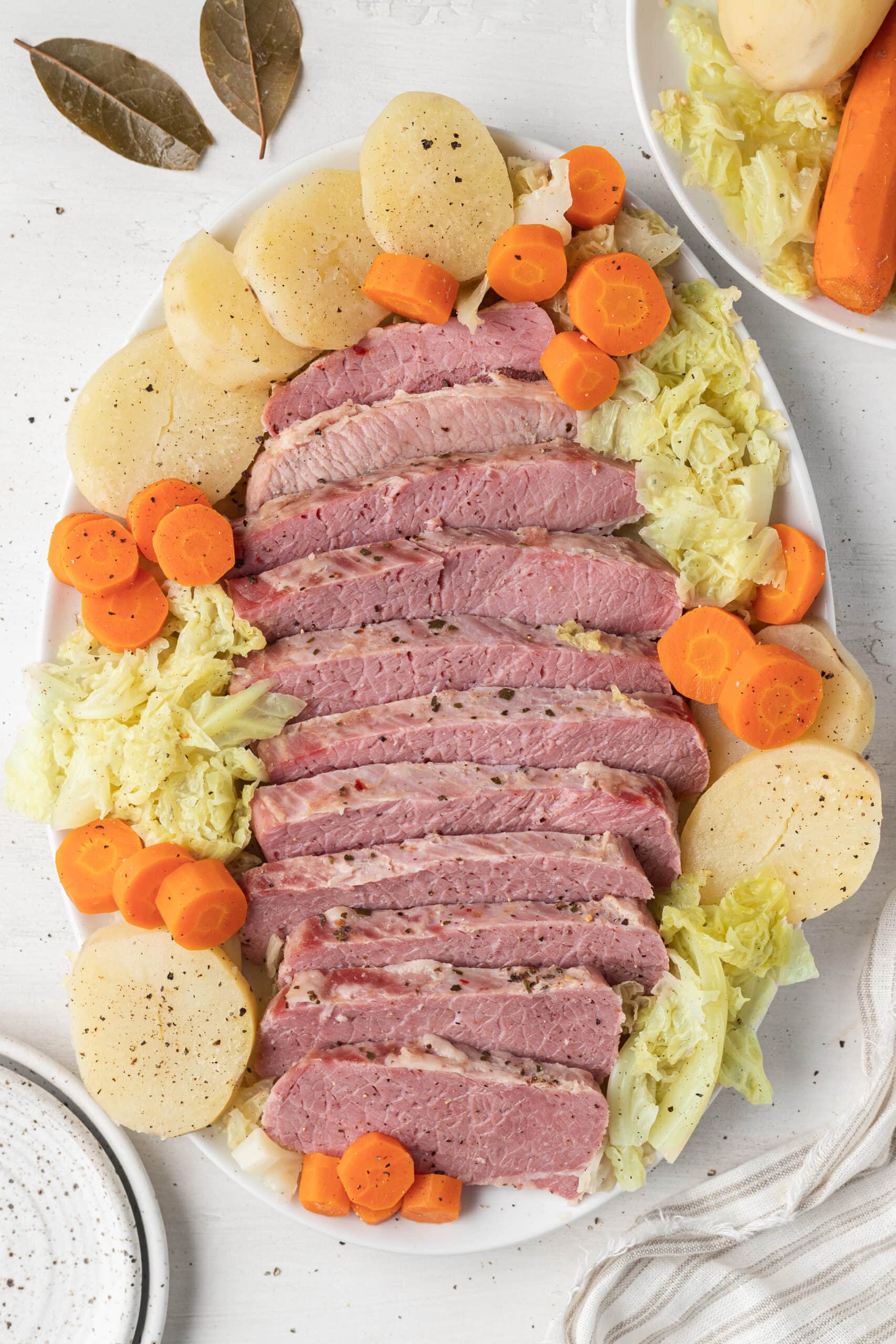 slow cooker corned beef on a white platter surrounded by cabbage, carrots and potatoes