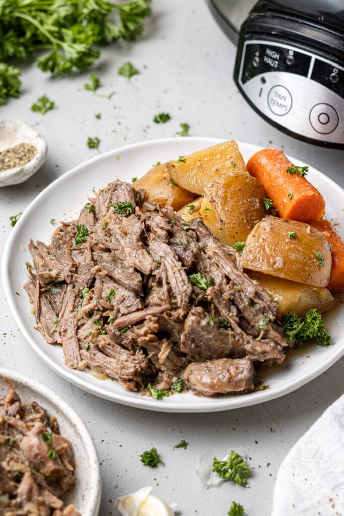 A plate of crock pot pot roast with carrots, herbs and potatoes