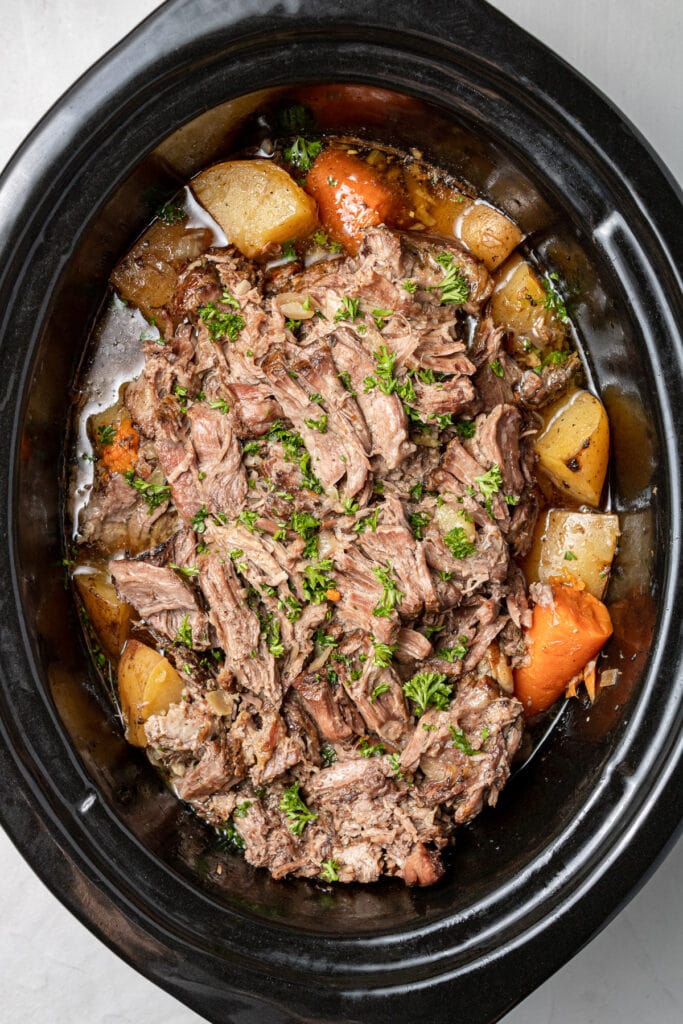 Cooked pot roast in a crock pot with carrots, potatoes and broth