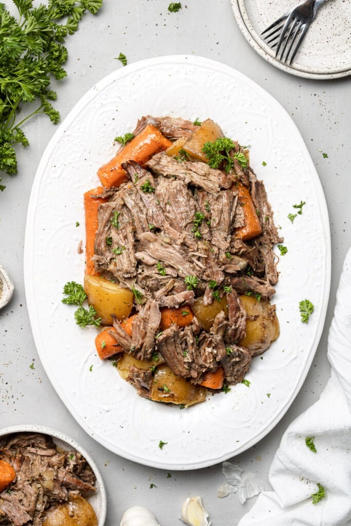 A white serving platter of slow cooker pot roast with carrots and potatoes