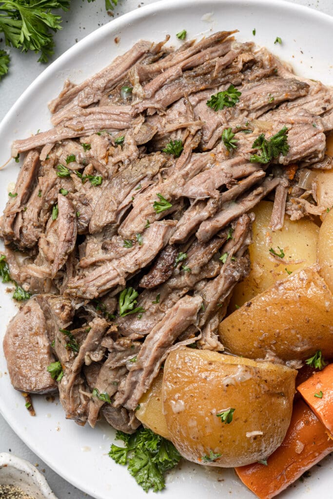 A close up of slow cooker pot roast on a plate with carrots and potatoes