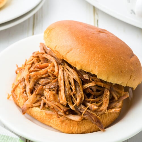 slow cooker pulled pork sandwich on a white plate on a white background