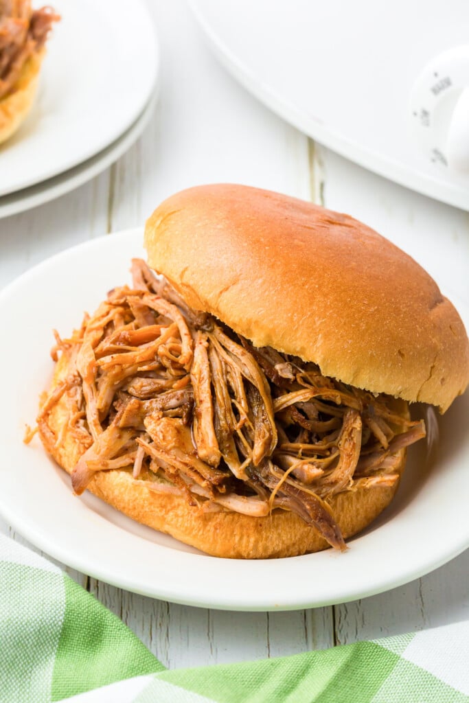slow cooker pulled pork on a bun on a white plate on a white background