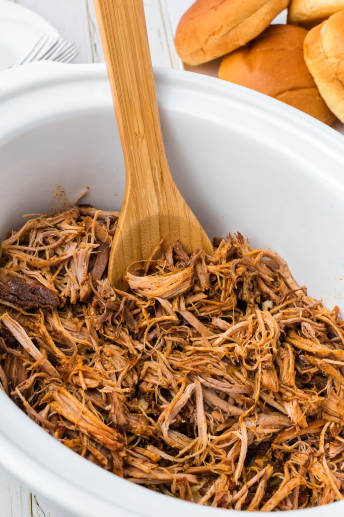 Slow Cooker pulled pork in a white crockpot after being shredded with a wooden spoon in the crockpot