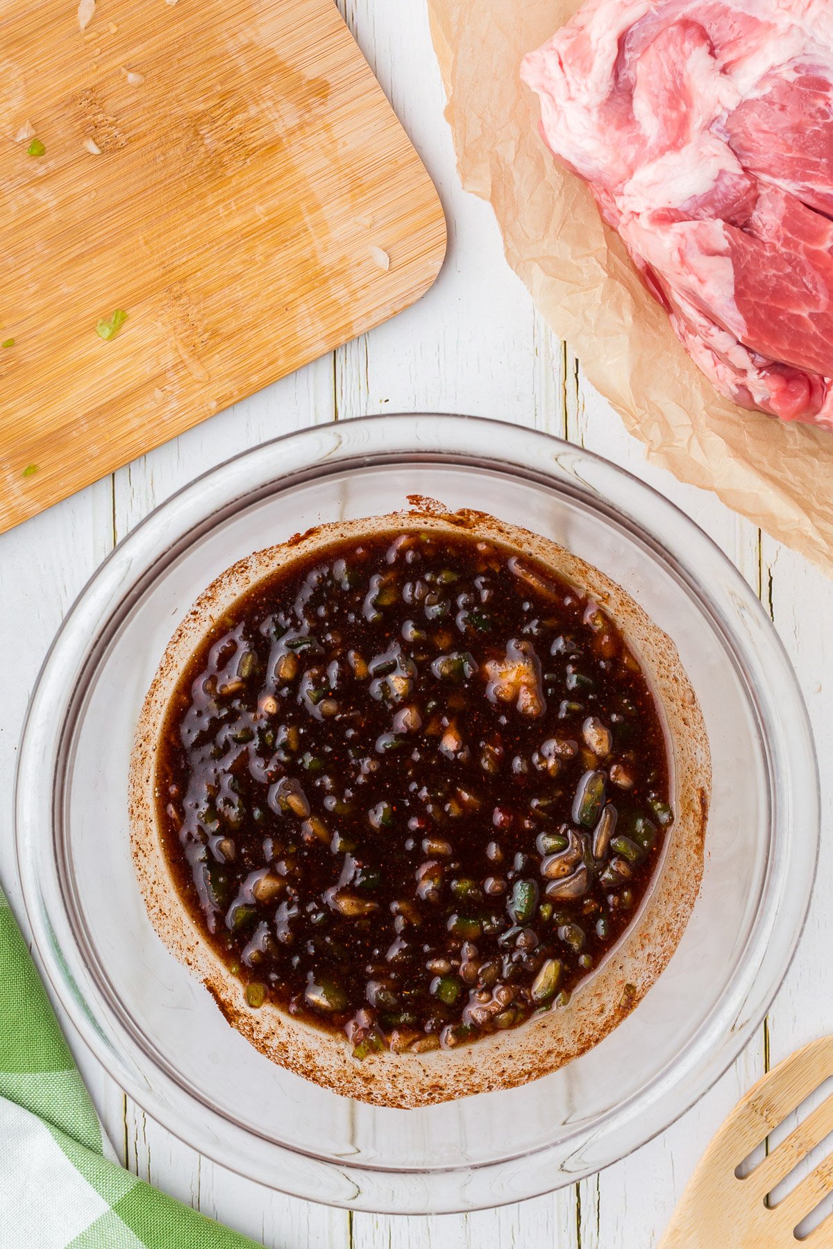 Sauce for slow cooker pulled pork (brown sugar, tomato paste, apple cider vinegar, chili powder, dry mustard, Worcestershire sauce, and smoked paprika) in a clear bowl with onions and peppers