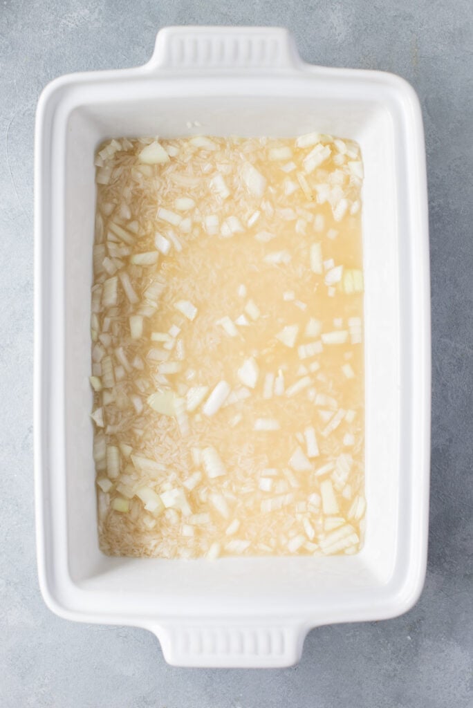 Some of the ingredients (white rice, minced garlic, onion and chicken broth) for mexican chicken casserole in a casserole dish stirred together