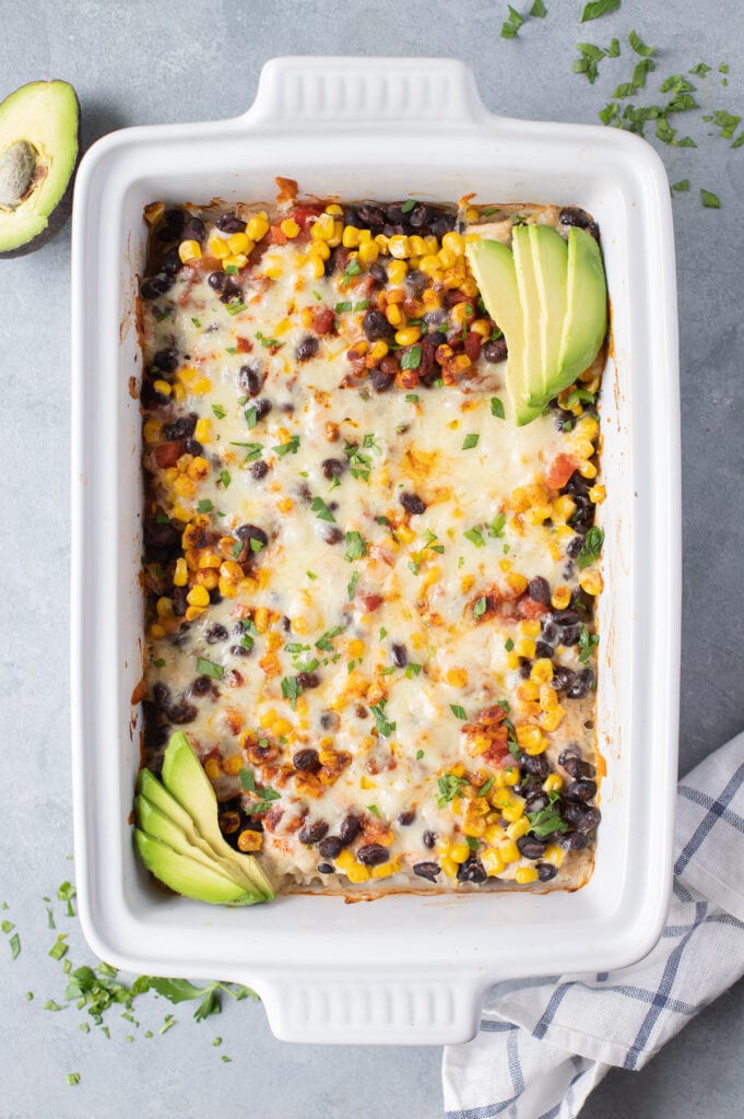 Freshly baked southwest chicken and rice casserole in a white casserole dish on top of a grey background with sliced avocado on the side