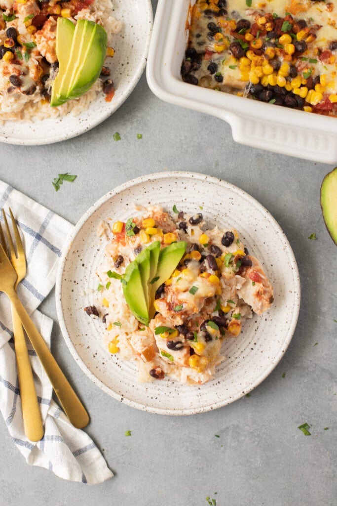 Cheesy Southwest Chicken Casserole on a white plate with a second dish and casserole dish off to the side