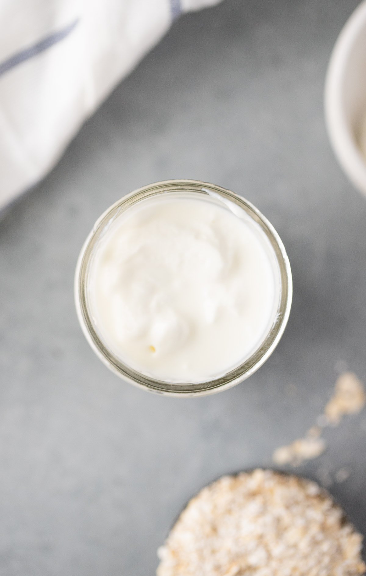 An overhead shot of a mason jar filled with overnight oats being prepared for strawberry overnight oats on a grey background