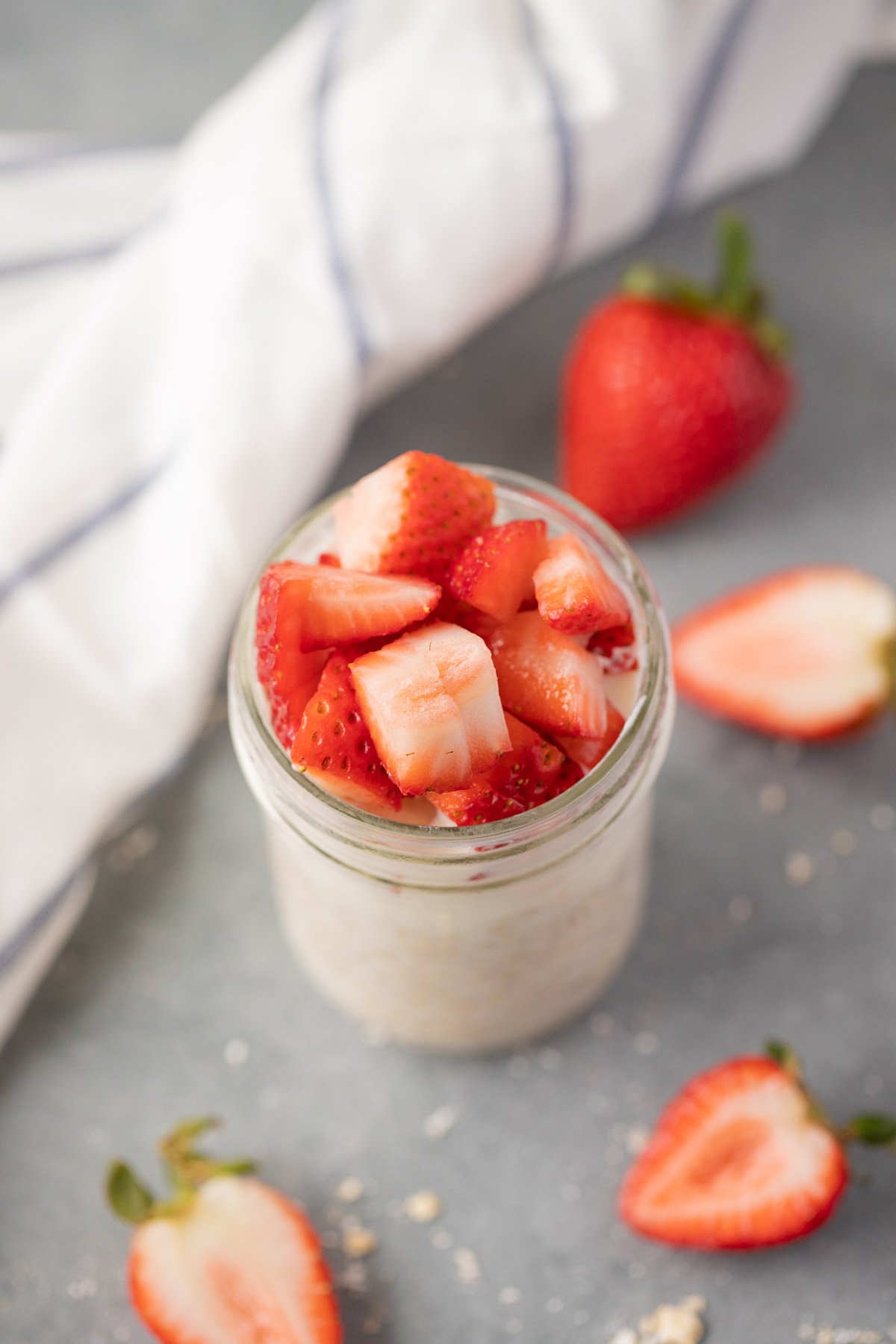 A shot of strawberry overnight oats in a mason jar on a grey background with chopped strawberries on the side