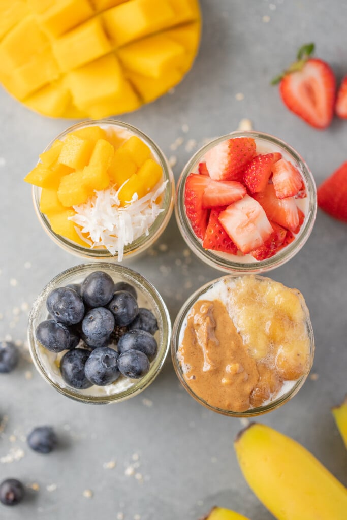 An overhead shot of four mason jars of overnight oats: mango overnight oats, strawberry overnight oats, blueberry overnight oats, banana overnight oats
