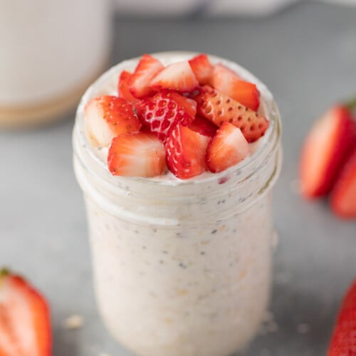 A mason jar of strawberry overnight oats on a grey background with strawberries on the side