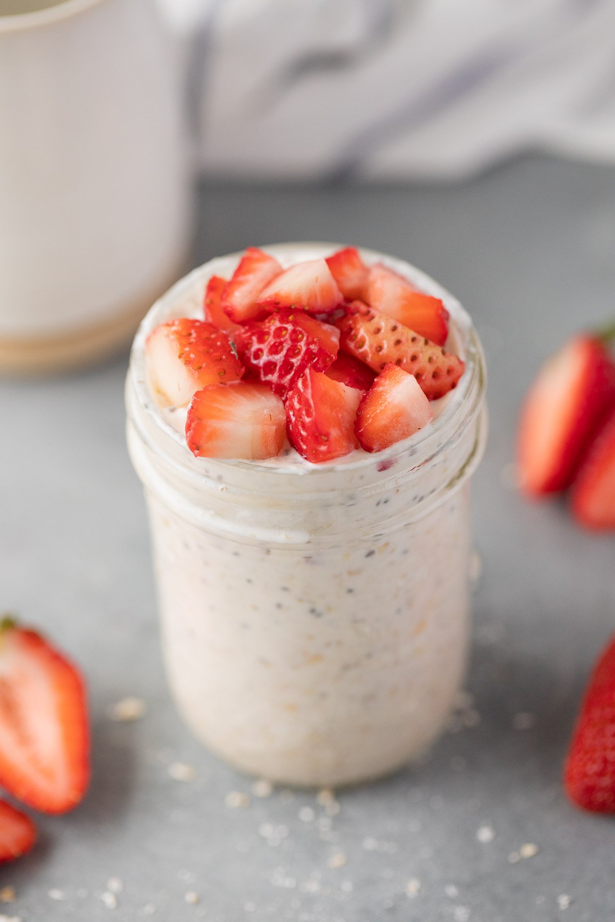 A mason jar of strawberry overnight oats on a grey background with strawberries on the side