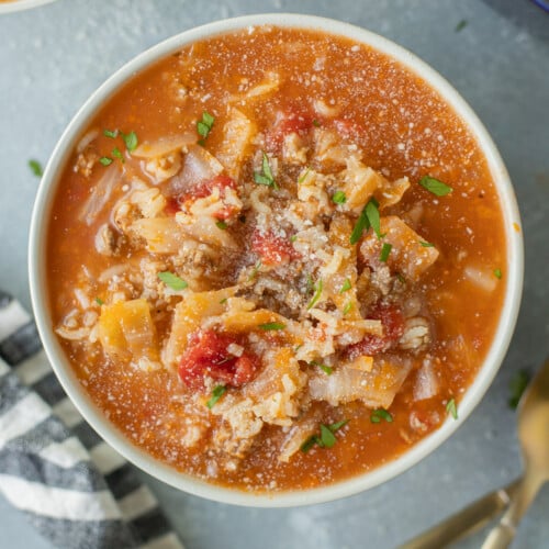 A bowl of hamburger cabbage soup with another bowl of soup and spoons on the side on a grey counter