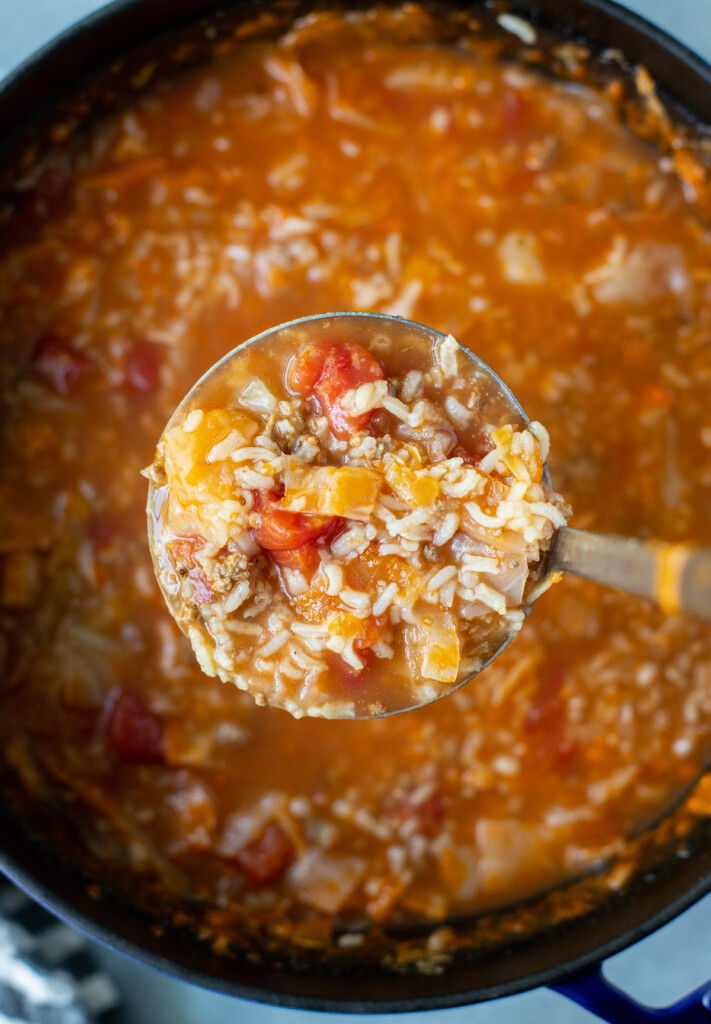 A ladle lifting a large scoop of cabbage roll soup out of a dutch oven of the soup