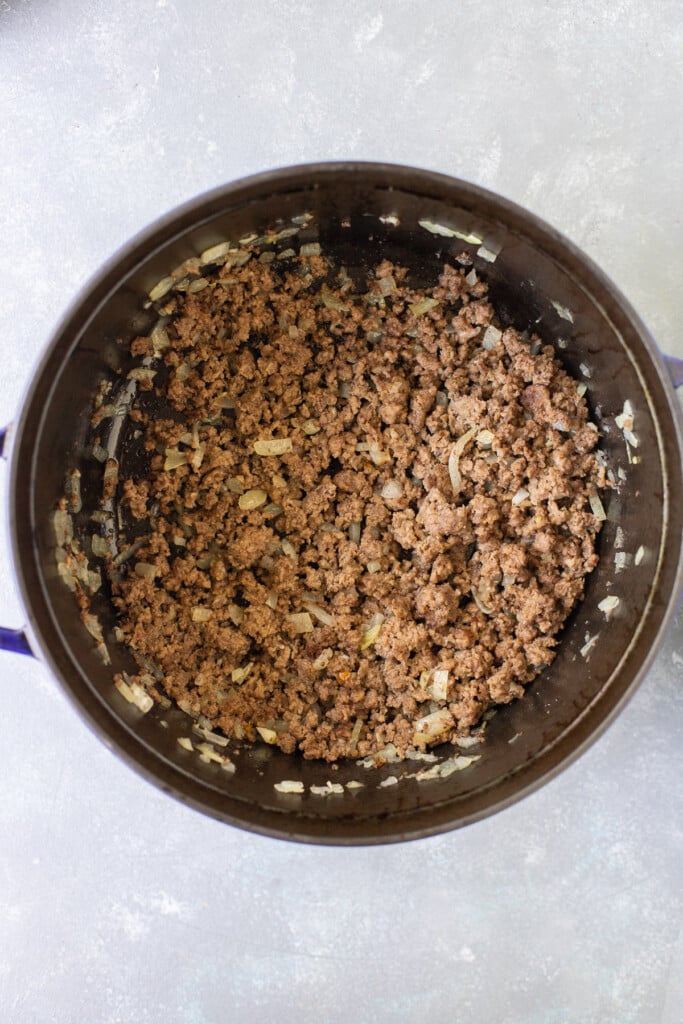 Ground beef, onion, and garlic sauteed in a dutch oven on a grey background