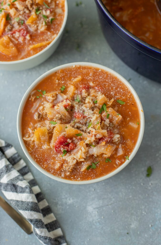 A bowl of stuffed cabbage soup with another bowl of soup and a dutch oven on the side on a grey counter