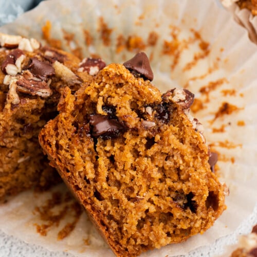 A halved sweet potato muffin with chocolate chips on a muffin paper on a white background