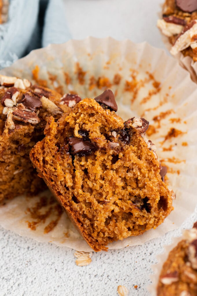 A halved sweet potato muffin with chocolate chips on a muffin paper on a white background