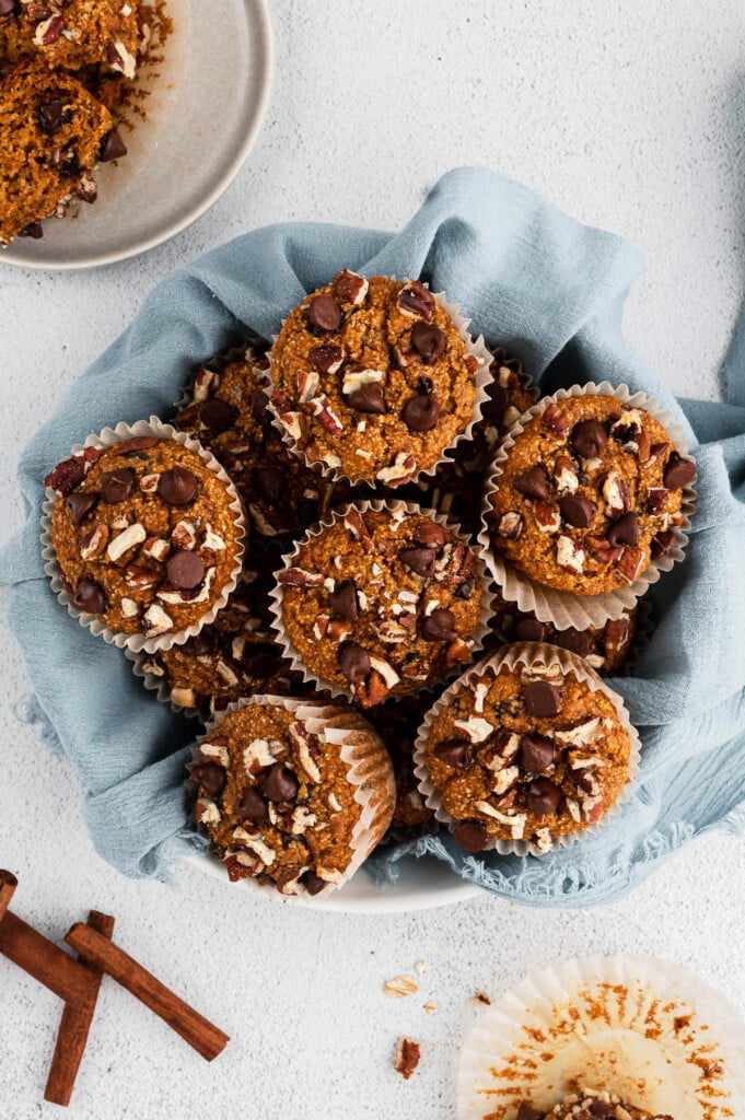 An overhead shot of a bowl of sweet potato muffins and a blue towel on a white background