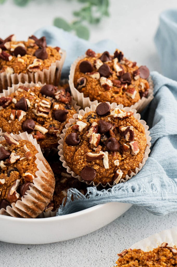 A white bowl with a blue cloth and sweet potato muffins in it on a white background