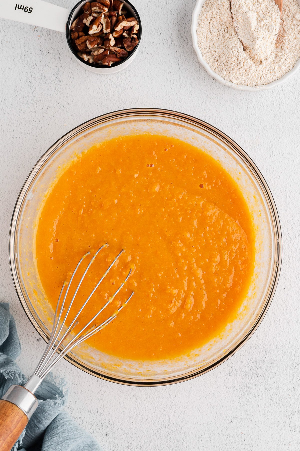 sweet potatoes, eggs, applesauce, milk, maple syrup, and vanilla extract being whisked in a clear bowl for healthy sweet potato muffins